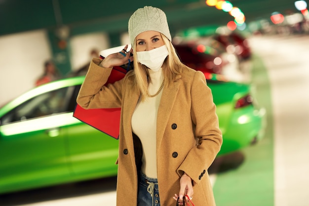 femme avec des sacs à provisions en masque dans un parking souterrain