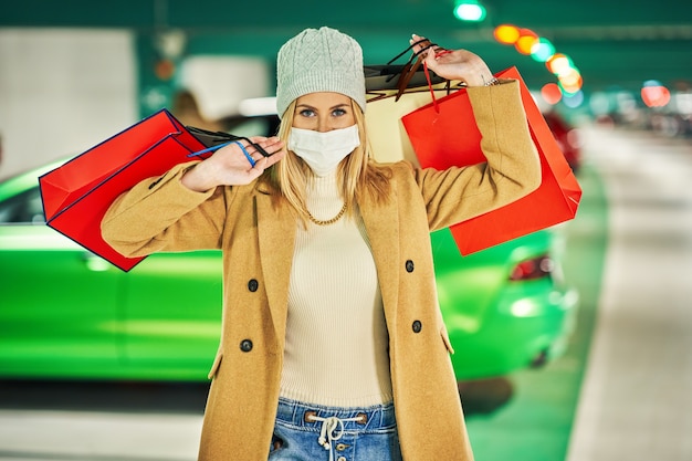 femme avec des sacs à provisions en masque dans un parking souterrain