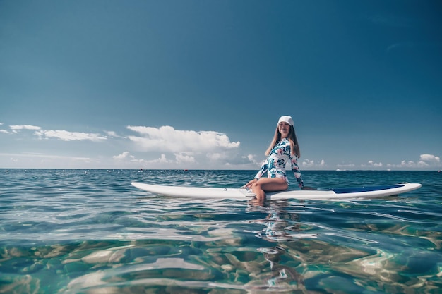 Femme saine et heureuse en bikini se reposant sur une planche de surf flottant sur la mer turquoise claire