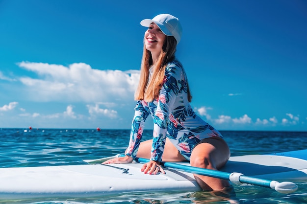 Femme saine et heureuse en bikini se reposant sur une planche de surf flottant sur la mer turquoise claire