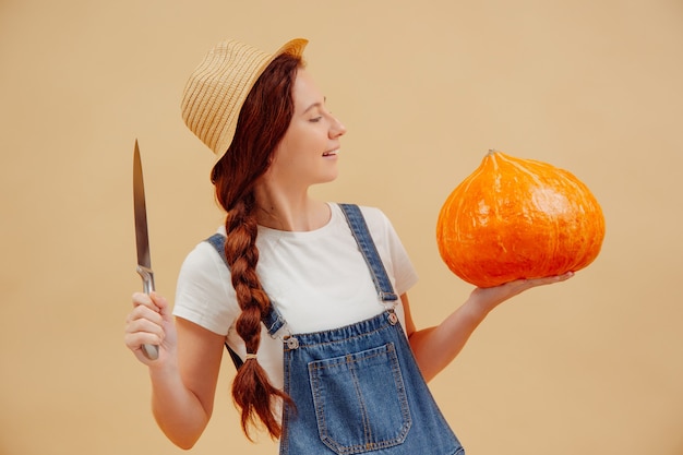 Femme en salopette avec un couteau tranchant sur fond jaune va couper la lanterne d'une citrouille