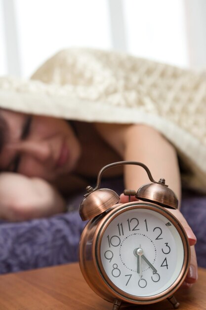 Une femme sans sommeil tend la main à contrecœur sous la couverture vers le réveil.