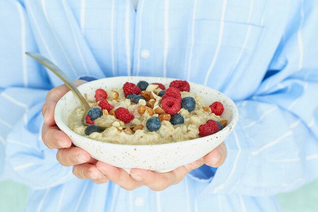 Femme sans visage tient dans les mains le petit-déjeuner, la bouillie d'avoine avec des baies et des noix