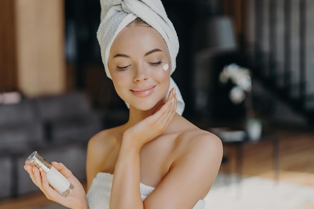 Une femme satisfaite applique une lotion pour le visage enveloppée dans une serviette met en valeur la beauté naturelle Concept de cosmétologie