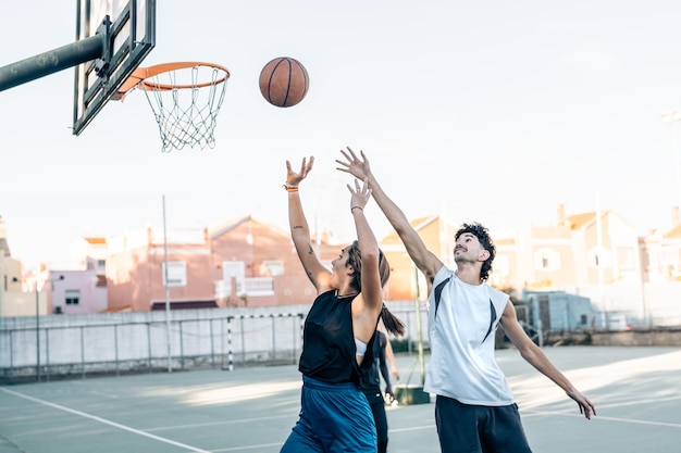 Femme sautant devant un homme tout en lançant une balle dans un panier en jouant au basket