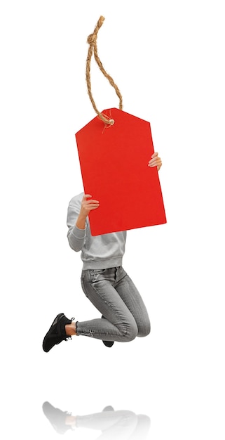 Femme sautant tenant une étiquette de vente rouge dans les mains. Isolé sur fond blanc.