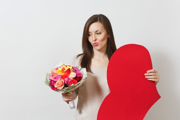 Femme sceptique tenant un grand coeur rouge, bouquet de belles fleurs roses sur fond blanc. Copiez l'espace pour la publicité. Place pour le texte. Concept de la Saint-Valentin ou de la Journée internationale de la femme.