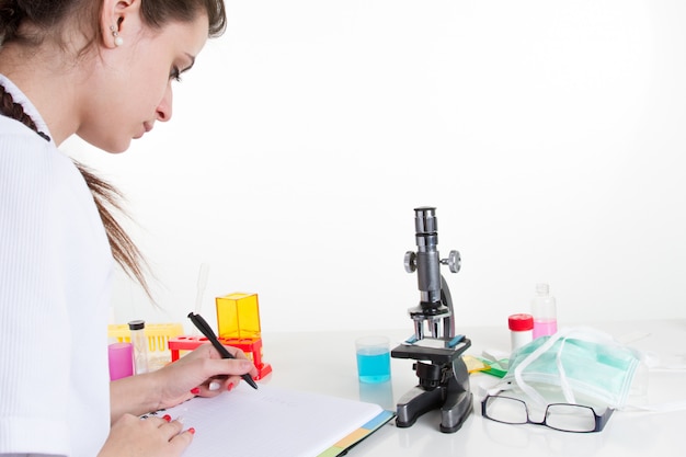 femme scientifique à l'aide de microscope et d'écriture dans le bloc-notes