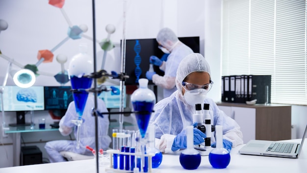 Femme scientifique en équipement de protection ajustant son microscope dans un laboratoire de chimie moderne.