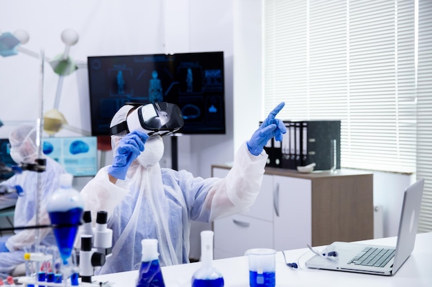 Femme scientifique portant des lunettes de réalité virtuelle pour simuler un test de recherche dans un laboratoire de chimie moderne.
