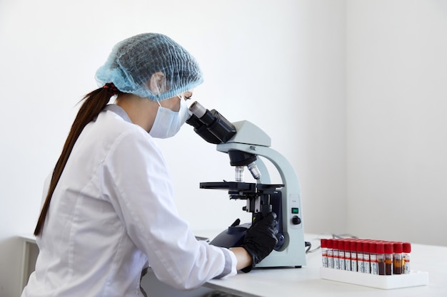 Femme scientifique regardant au microscope dans un laboratoire chimique moderne faisant des recherches