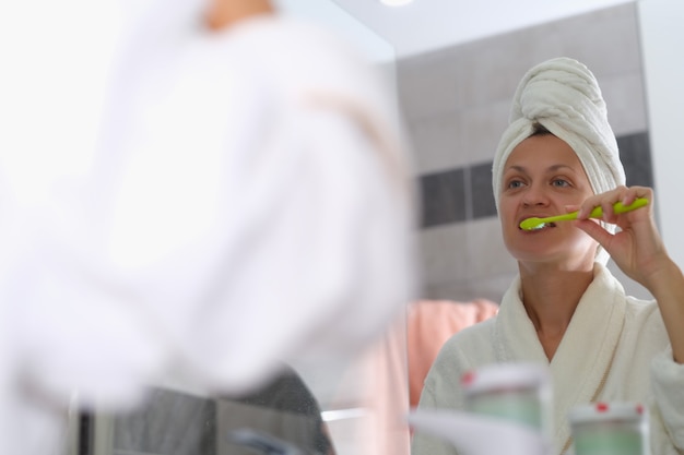 La femme se brosse les dents devant le miroir agrandi