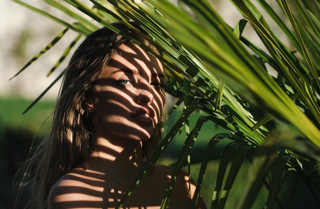 Femme se cachant derrière les feuilles de palmier belle jeune femme visage avec des ombres de feuille de palmier tropical