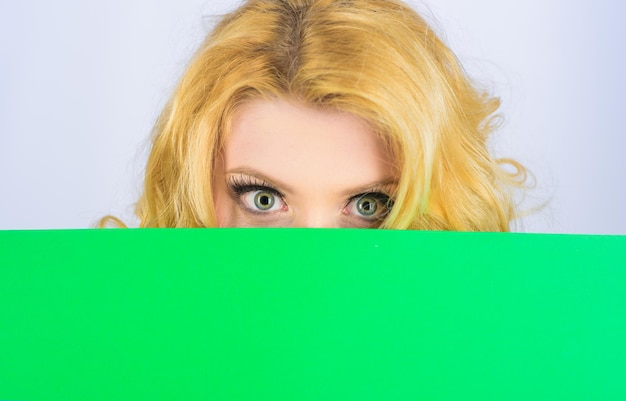 Femme se cachant derrière un panneau d'affichage femme sérieuse avec une affiche vierge de panneau d'affichage vierge fille blonde furtivement