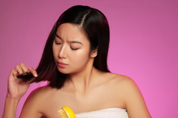 Une femme se coiffant les cheveux avec un peigne jaune sur un fond rose vibrant pendant une séance de beauté.