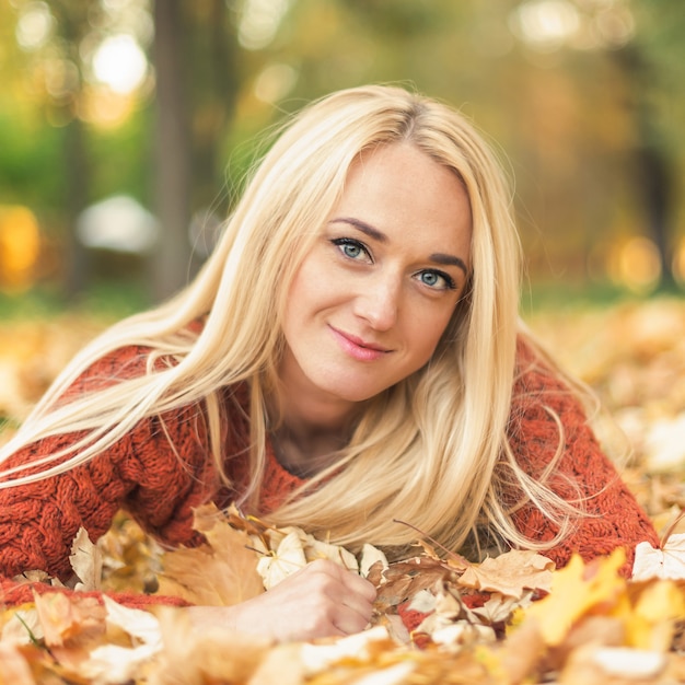 La femme se couche sur des feuilles au parc d'automne