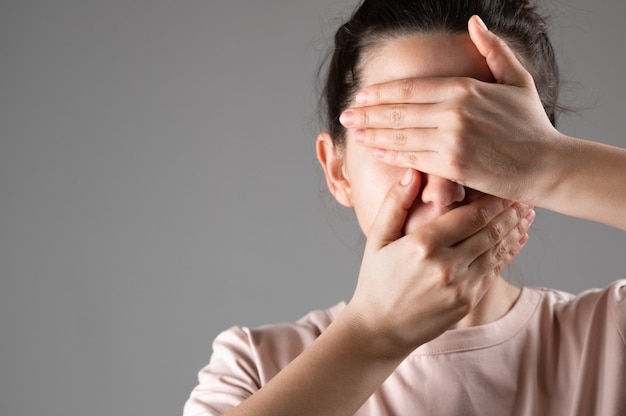 La femme se couvre la bouche et les yeux avec ses mains.