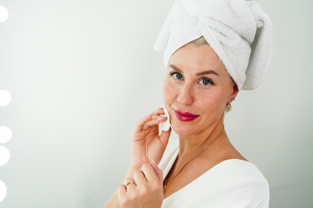 Une femme se démaquille avec une serviette dans la salle de bain s'essuie le visage avec un coton démaquillant et ...