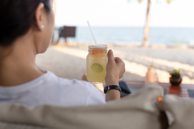 Femme se détendre sur la plage avec verre à la main verre de miel citron frais.