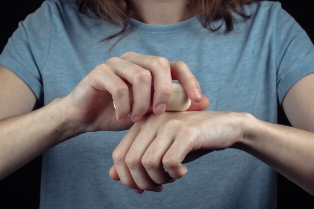 Femme se lave les mains avec du savon sur un mur noir.