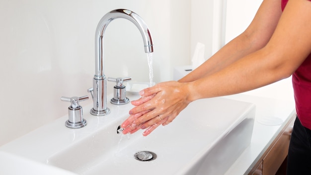 Femme se laver les mains sous l'eau courante dans un lavabo blanc