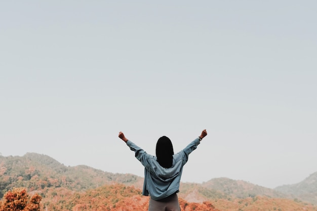 La femme se lève les mains vers le concept de liberté du ciel avec un ciel bleu et un fond de montagne de champ d'été.