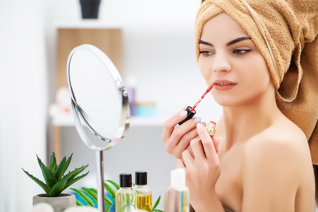 Femme se prépare pour le travail faisant le maquillage du matin dans le miroir de salle de bain à la maison