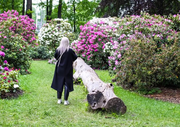 Une femme se promène dans un jardin fleuri et arboré.