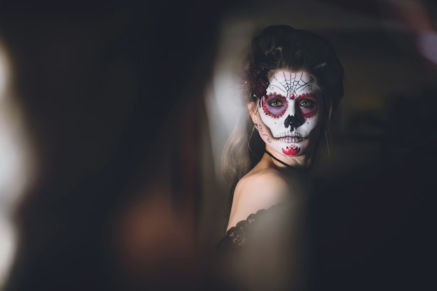 Femme se regardant dans le miroir avec son visage habillé pour le carnaval