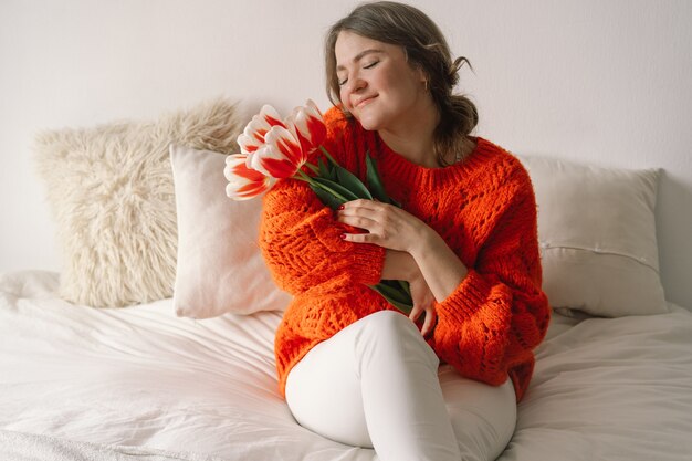 La femme se réjouit des tulipes. Belle femme assise sur le lit