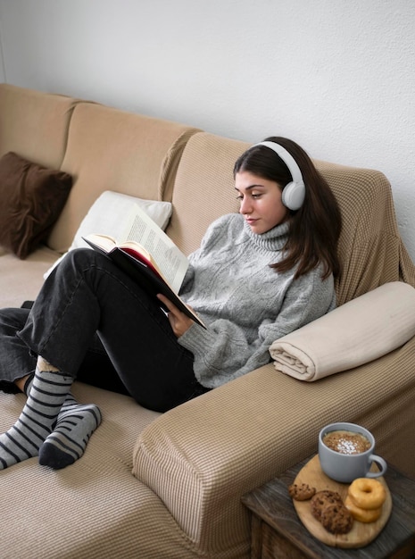 Femme se relaxant en lisant un livre et prenant une collation allongée sur le dos sur un canapé confortable