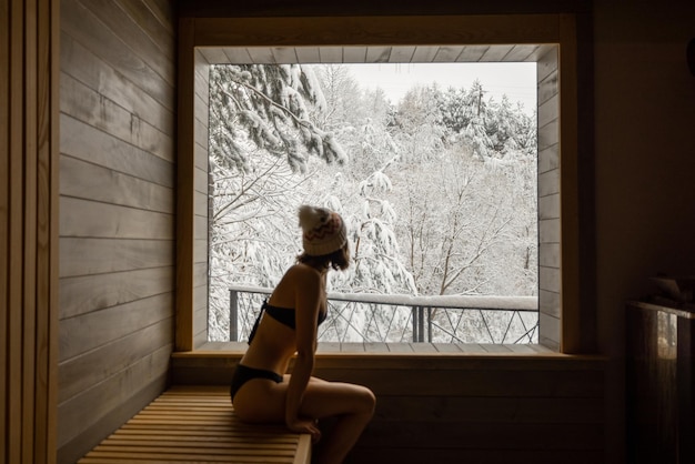 Femme se reposant dans un sauna avec vue sur la nature enneigée