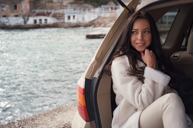 Une femme se reposant à l'intérieur du coffre d'une voiture et face à la mer