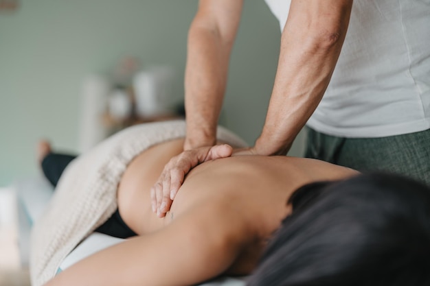 Une femme se repose sur une civière pendant qu'un physiothérapeute réchauffe ses muscles avec ses mains