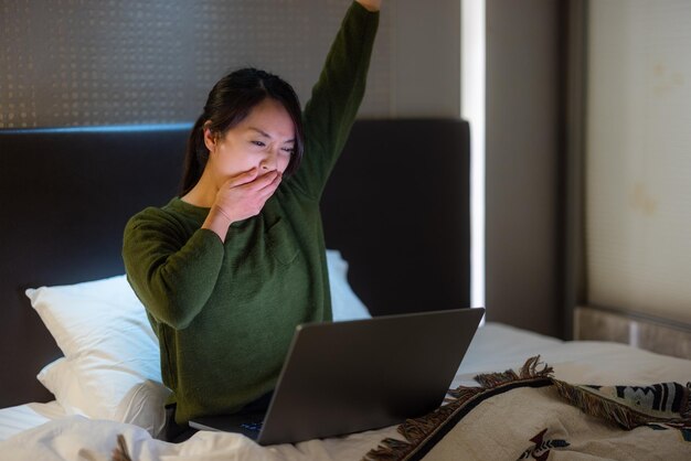 La femme se sent fatiguée de travailler à l'ordinateur avec assis sur le lit la nuit