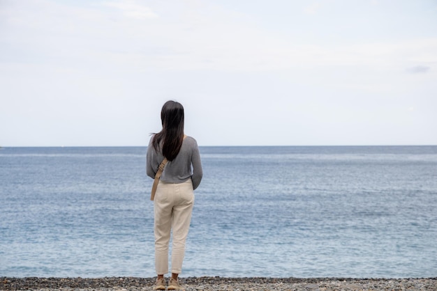 Une femme se tient à côté de la plage et profite de la vue.