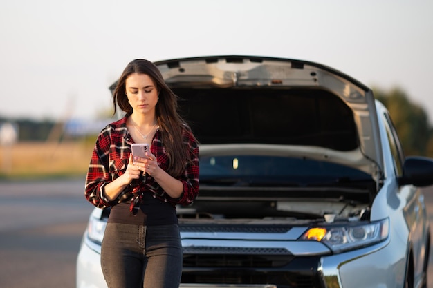 Une femme se tient à côté de sa voiture en panne avec une tasse de café à la main.