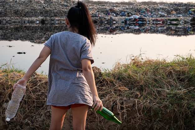 la femme se tient dans la main avec une bouteille en verre vert et une bouteille en plastique transparent