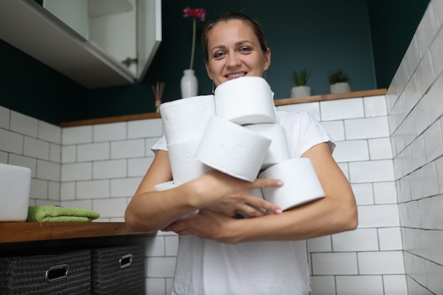Photo femme se tient dans les toilettes et tient la pile de rouleaux de papier toilette dans ses mains.