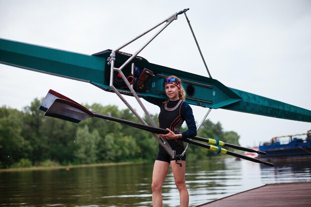 La femme se tient debout posant manipulant un kayak et riant sur la rive du fleuve