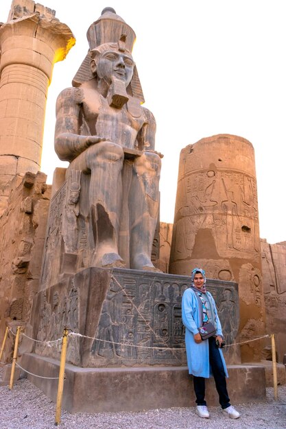 Photo une femme se tient devant une statue d'un dieu égyptien assis.