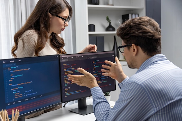 Une femme se tient en face d'un programmeur travaillant sur un bureau pour discuter du postulat.