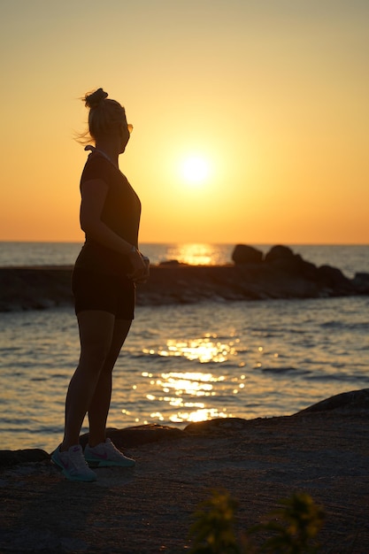 Une femme se tient sur une plage devant un coucher de soleil.