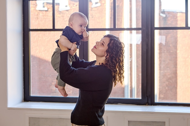 La femme se tient près de la fenêtre avec le petit garçon dans des mains