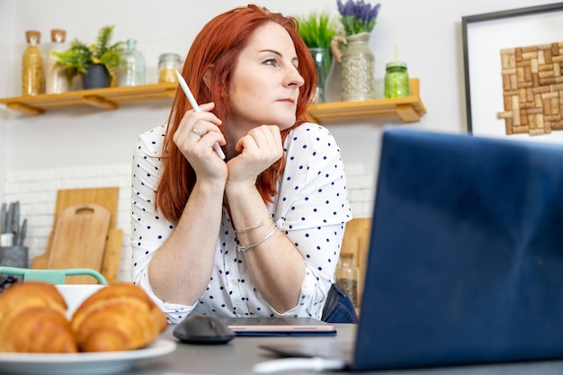 une femme séduisante est assise devant un ordinateur dans une cuisine un blogueur écrit un article sur du contenu internet