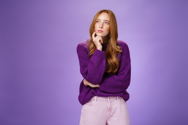 Une femme séduisante, intelligente et créative, réfléchie et concentrée, aux cheveux roux et aux taches de rousseur plissant les yeux, regardant le coin supérieur gauche tout en pensant avoir une idée ou un plan tenant la main sur le menton comme choix.