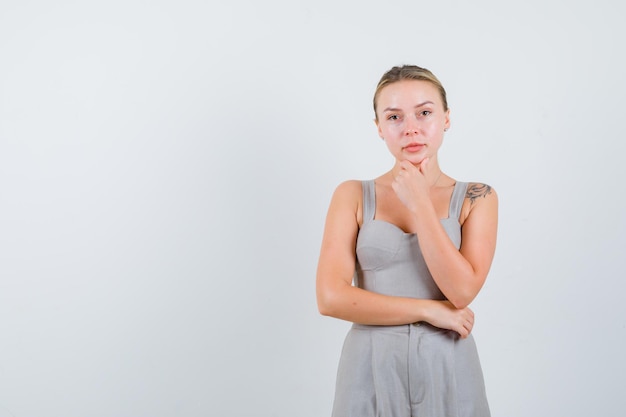 Une femme séduisante a mis la main sur le menton en costume gris coupe-bas avec tatouage et a l'air sérieux