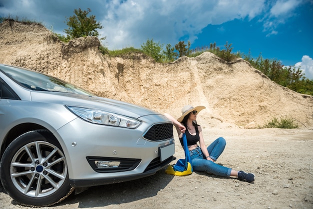 Femme séduisante posant près de la voiture en été à l'extérieur de la ville jouissant de la liberté