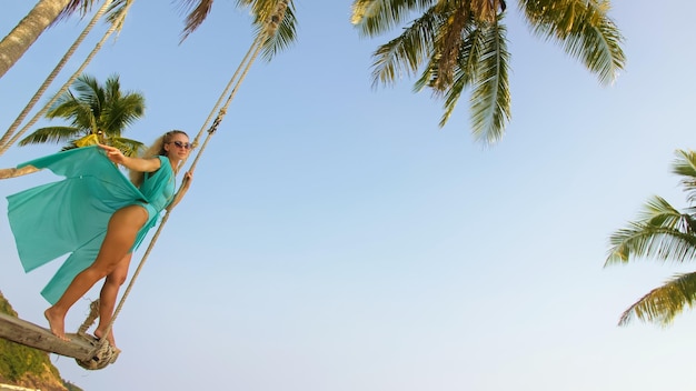 Femme séduisante se balançant sur une balançoire sur une plage tropicale au bord de la mer turquoise concept