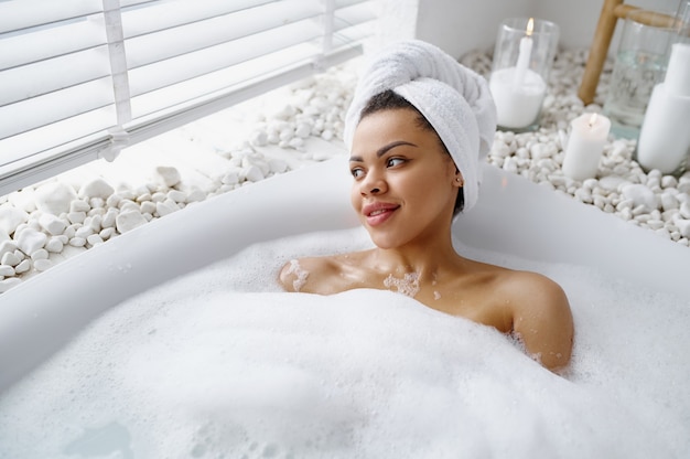 Une femme séduisante se détend dans un bain moussant. Personne de sexe féminin dans la baignoire, soins de beauté et de santé au spa, traitement de bien-être dans la salle de bain, cailloux et bougies sur fond
